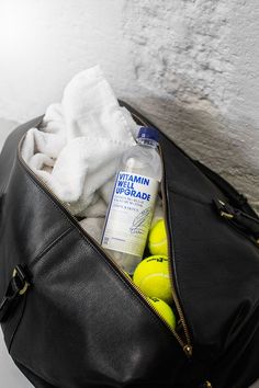 a duffel bag filled with tennis balls and personal care items next to a brick wall