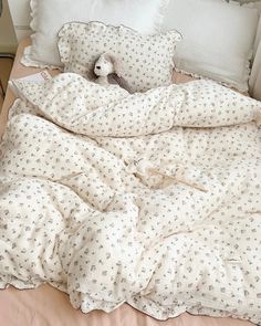 an unmade bed with a teddy bear sitting on top of the comforter and pillows