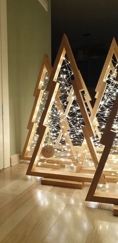 three wooden christmas trees with lights on them in the middle of a wood floored room