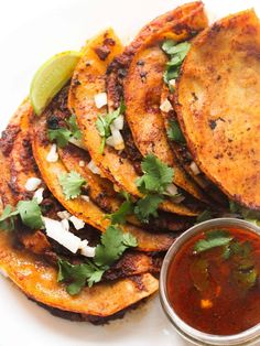 some tacos are sitting on a plate with sauce and cilantro in the background