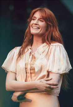 a woman with red hair is smiling and holding her arms crossed in front of her chest