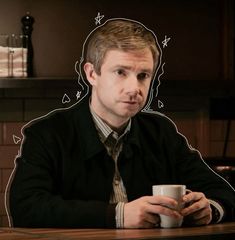 a man sitting at a table with a coffee cup in front of his face,