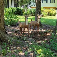 two statues of deer in front of a house with trees and bushes around them,