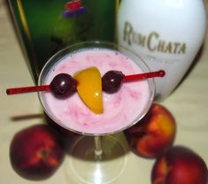 a drink in a glass with two cherries on the rim and a bottle next to it