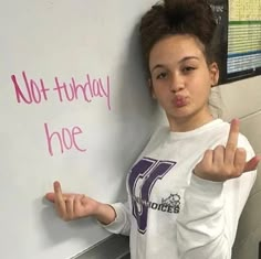 a girl standing in front of a whiteboard with writing on it and making the peace sign