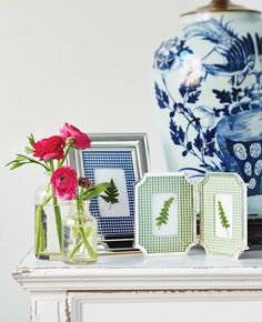 three vases with flowers in them sitting on a table next to pictures and frames