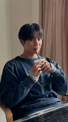 a young man sitting at a table drinking from a straw