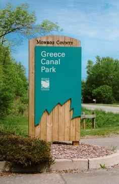 a wooden sign sitting on the side of a road next to a lush green field