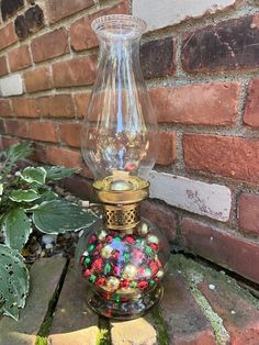 a glass vase filled with lots of colorful beads sitting on top of a brick wall