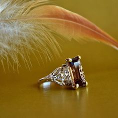 a close up of a ring on a table with a feather in the foreground