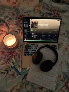 an open laptop computer sitting on top of a bed next to a candle and notebook