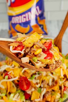 a wooden spoon full of taco salad with tortilla chips on the side