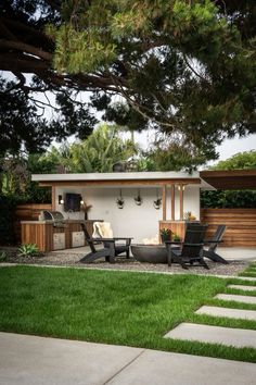 an outdoor living area with chairs, table and grill in the middle of green grass