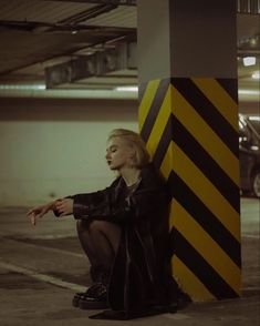 a woman sitting on the ground next to a tall yellow and black striped pole in an empty parking garage