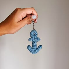 a hand holding a blue crocheted key chain with an anchor on the end