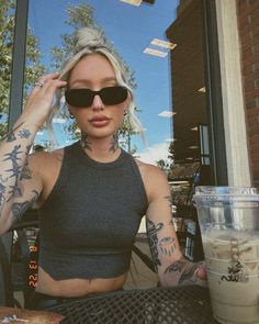 a woman sitting at a table with a drink in front of her and tattoos on her arms