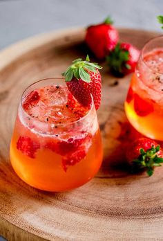 two glasses of strawberry black pepper gin and tonic sitting on a wooden tray with strawberries