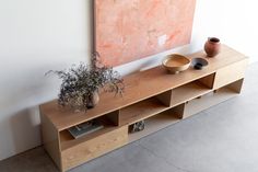 a wooden shelf with vases and bowls on it next to a wall mounted painting