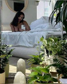 a woman sitting on top of a bed surrounded by potted plants and greenery