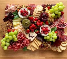 an assortment of cheeses, meats and fruit on a platter with grapes