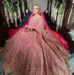 a woman in a pink and gold wedding gown sitting on stairs with flowers behind her