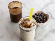 two drinks are sitting next to each other on a marble table with spoons and chocolate beans