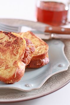 two pieces of french toast on a plate with a cup of tea in the background