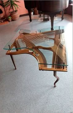 a glass and metal coffee table in the middle of a room with piano behind it