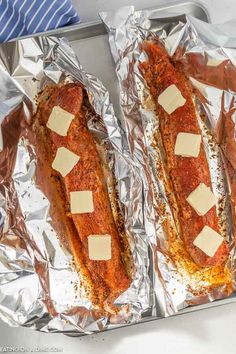 two hot dogs covered in cheese and seasoning sitting on tin foil