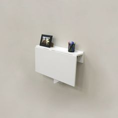 a white wall mounted shelf with two pictures on it and a pen holder next to it