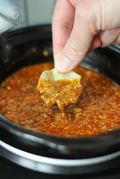 a person dipping some food into a crock pot filled with chili and cheese sauce