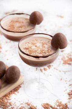 two glasses filled with milkshakes and topped with chocolate candies on a white surface