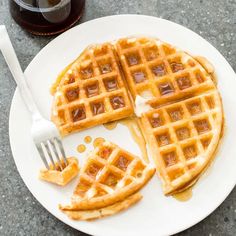 two waffles on a white plate with syrup and a fork next to them