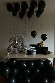 black balloons are hanging from the ceiling near a table with a cake and some flowers