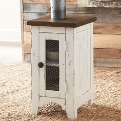 a white cabinet sitting on top of a rug next to a wooden table with a vase