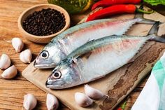 two fish sitting on top of a wooden cutting board next to garlic and peppercorst