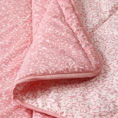 a pink and white bed spread with leaves on it