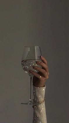 a woman's hand holding a wine glass in front of her face with glitter on it