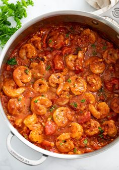 a pot filled with shrimp and tomato sauce on top of a counter next to parsley