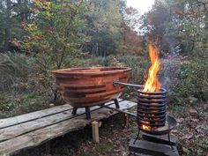 a large bowl sitting on top of a wooden bench next to a fire pit in the woods