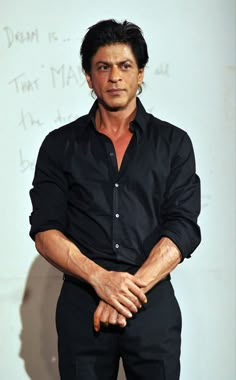 a man in black shirt and pants standing next to a wall with writing on it