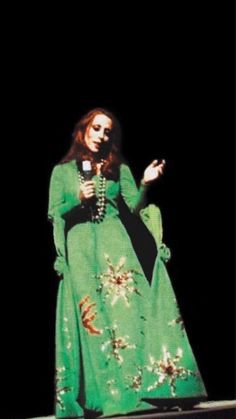 a woman in a long green dress standing on stage with her hands out to the side