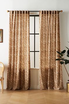 a living room with a chair and window covered in gold sequin curtain panels next to a potted plant