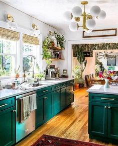 a kitchen with green cabinets and white counter tops is pictured in this image, there are many potted plants on the window sill