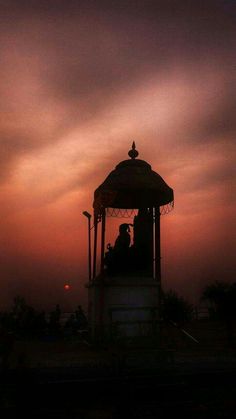 a gazebo with people sitting on it at sunset