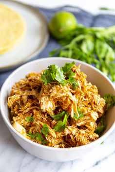 a white bowl filled with shredded chicken and garnished with cilantro