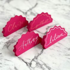 pink place cards with names on them sitting on a marble countertop in front of a marble background