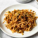 a white plate topped with shredded carrots next to a cup of coffee and sauce