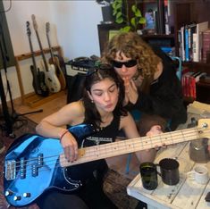 two women sitting on the floor playing with a blue guitar and another woman standing next to her