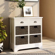 a white cabinet with wicker baskets next to a potted plant and pictures on the wall